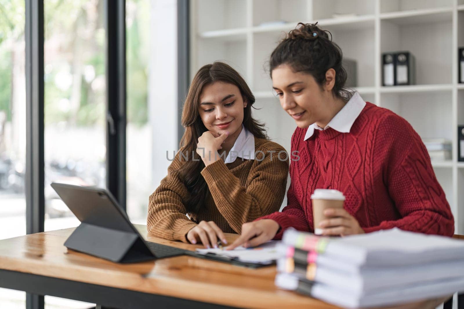 Two diverse female smiling while working together at a boardroom table during a meeting in a modern office.