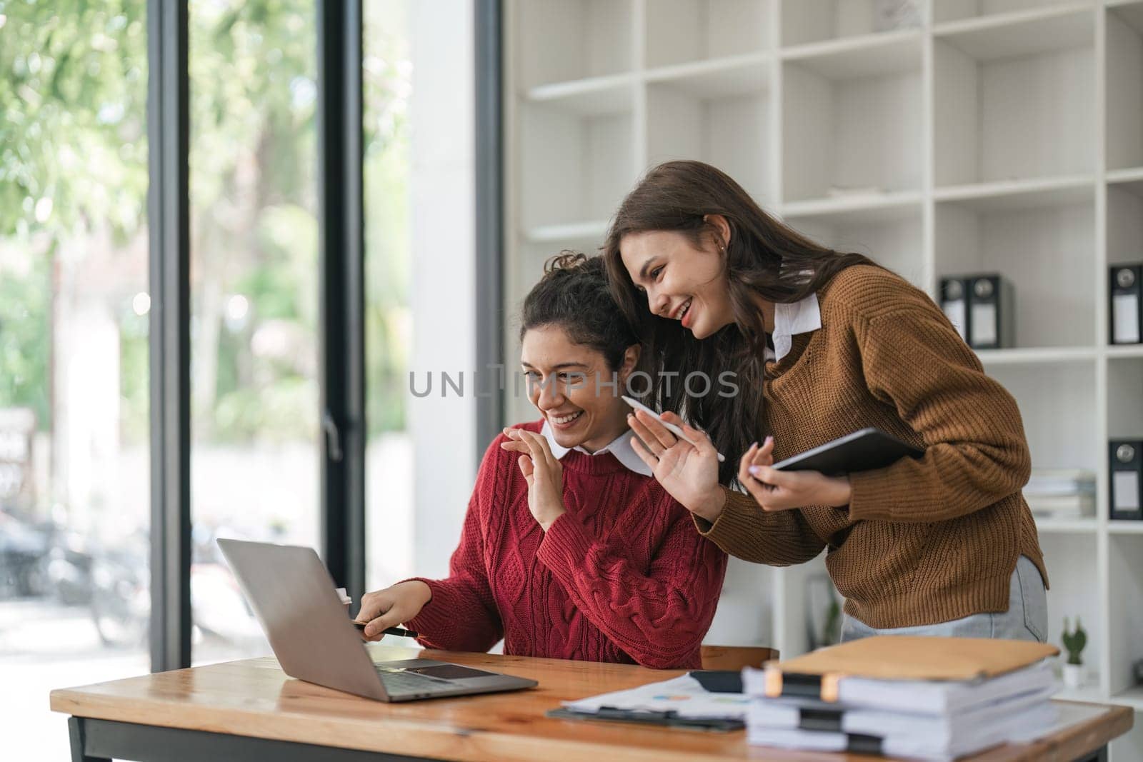 Two diverse female smiling while working together at a boardroom table during a meeting in a modern office by nateemee