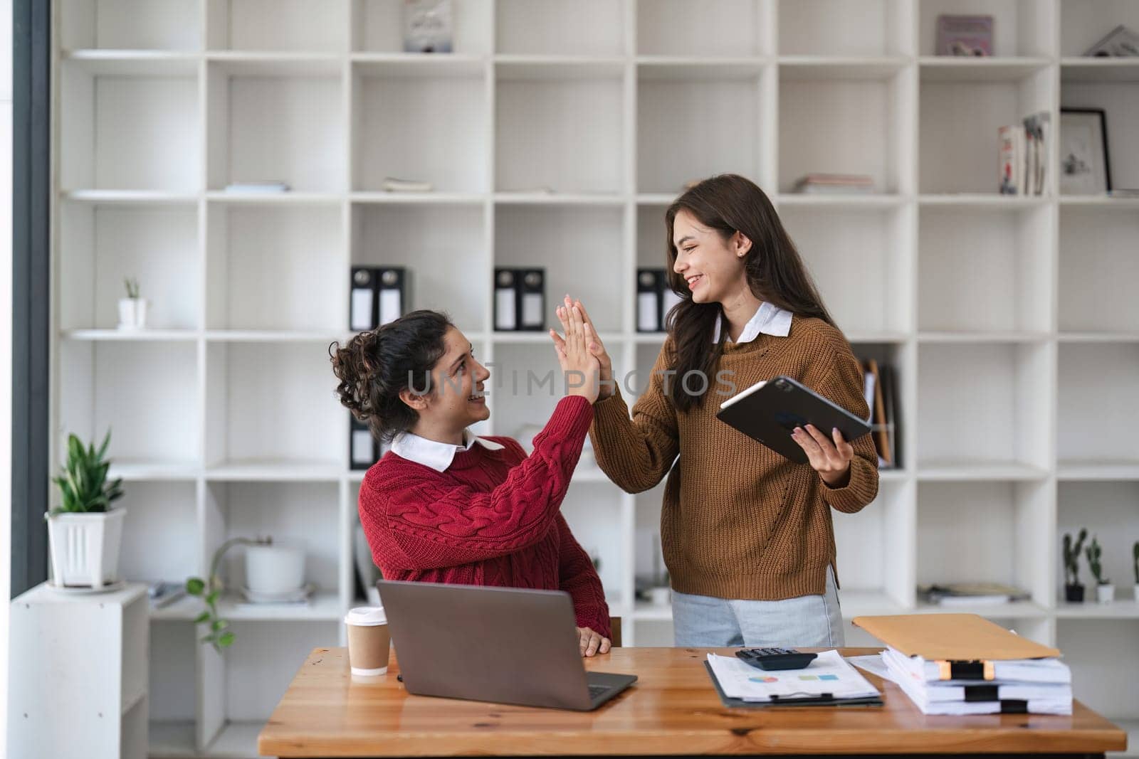 Successful business people giving each other a high five in a meeting. Two young business celebrating teamwork in an office..
