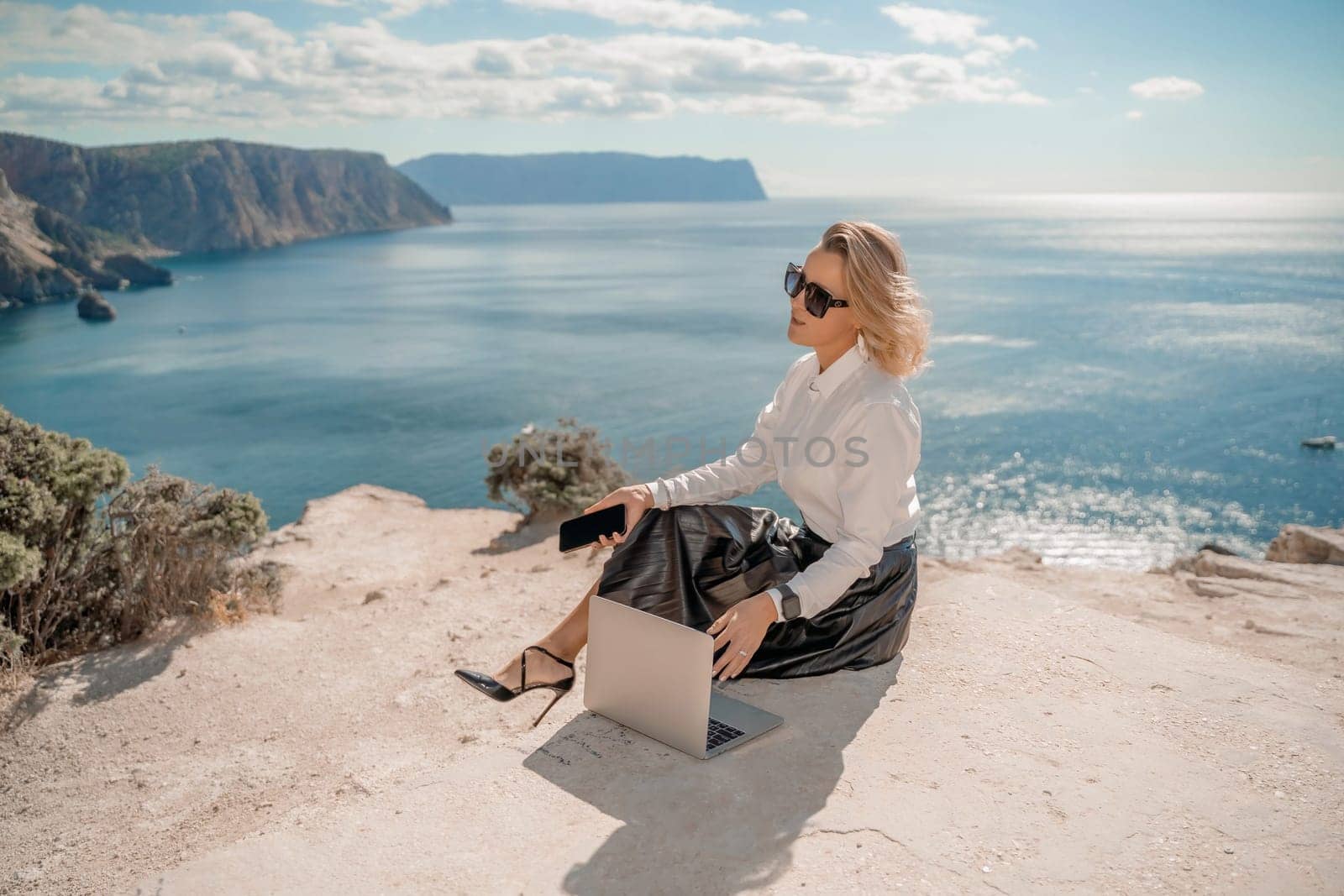 Freelance women sea working on a computer. Pretty middle aged woman with computer and phone outdoors with beautiful sea view. The concept of remote work