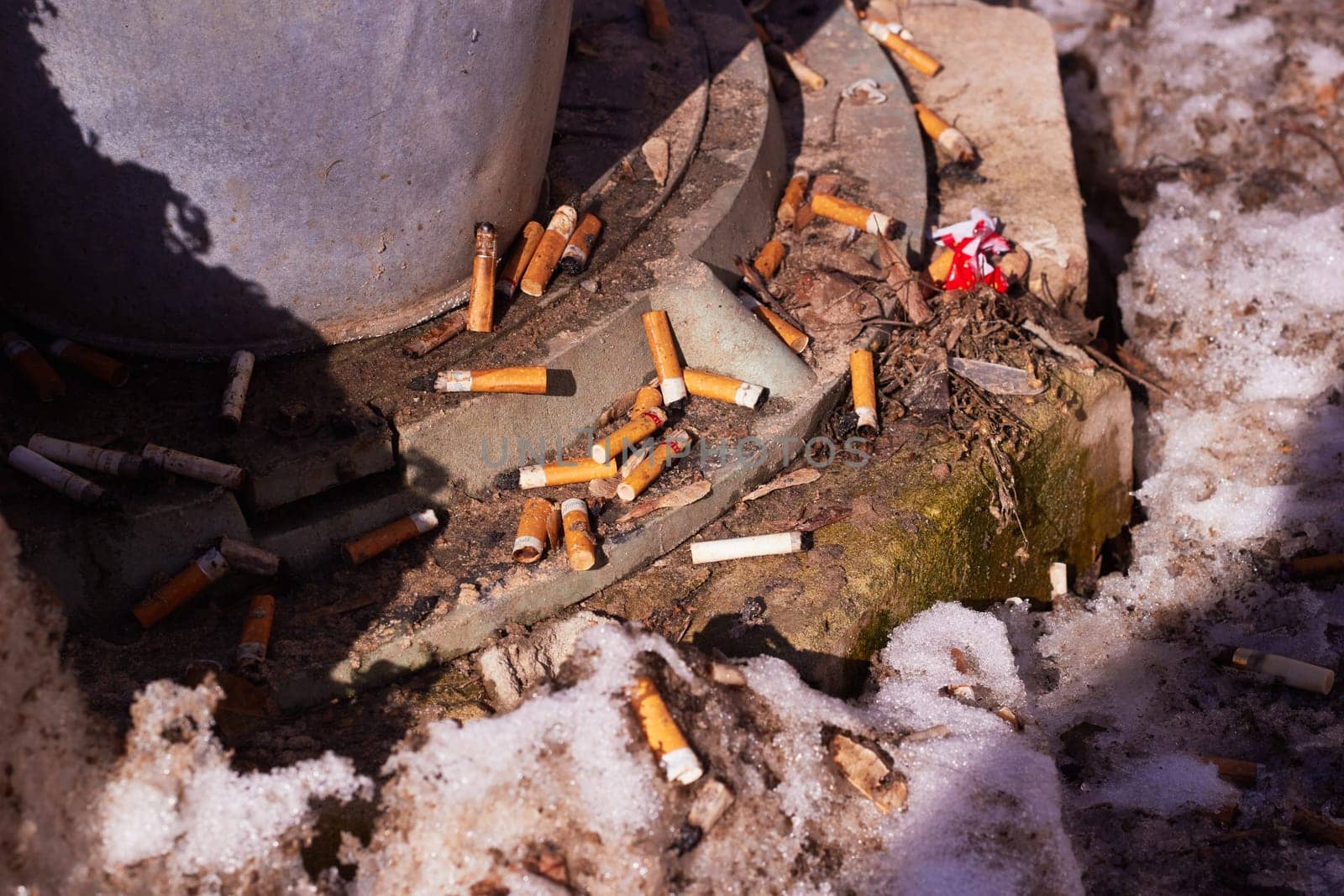 A lot of cigarette butts next to the manhole cover after the snow melts. Landscaping. Garbage. Environmental pollution. Harm to health. Environmental problems.