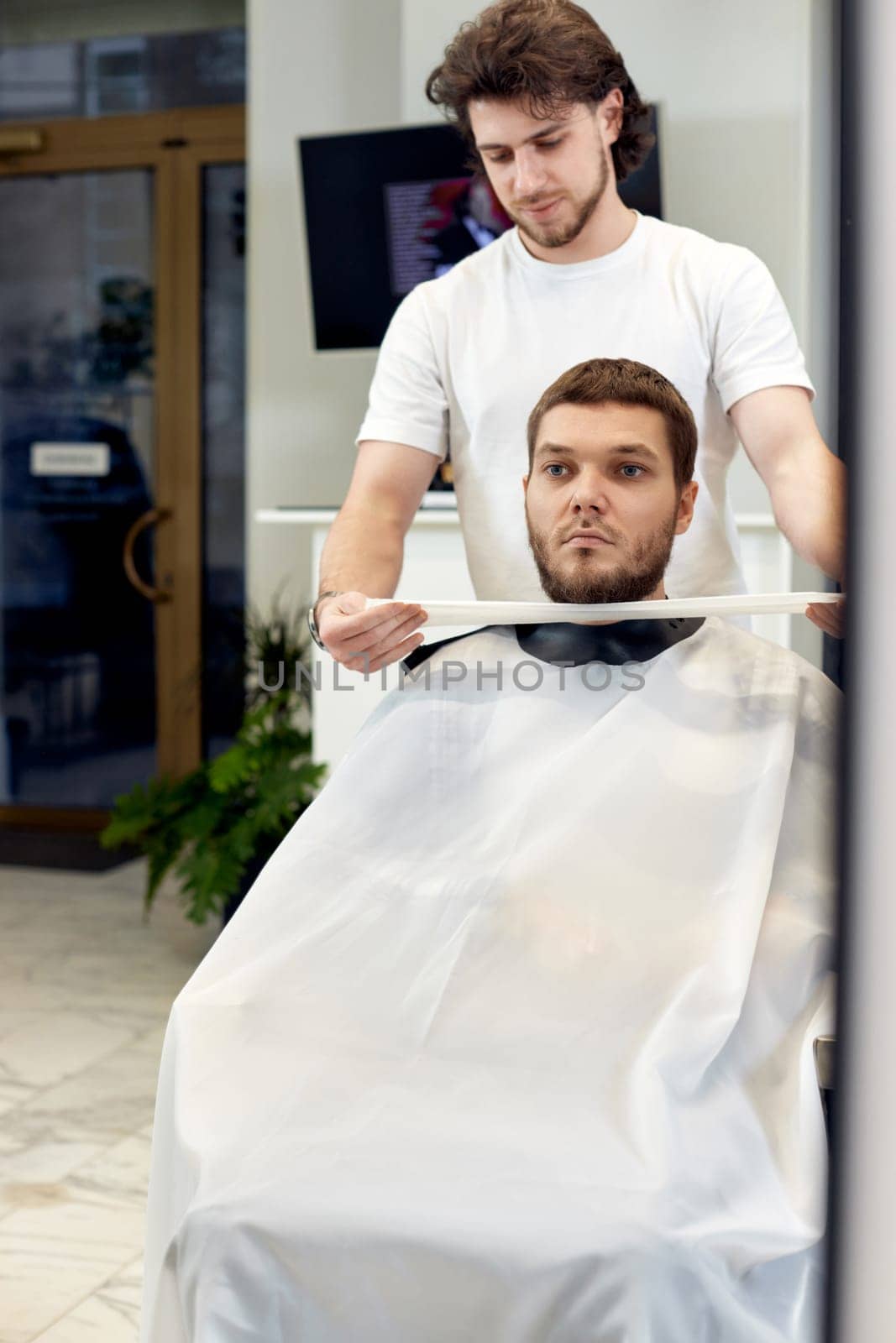 Barber and caucasian client man in front of the mirror in barber shop