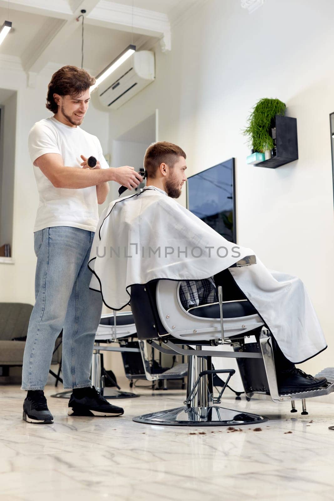 Barber trim hair with clipper on handsome bearded man in barber shop.
