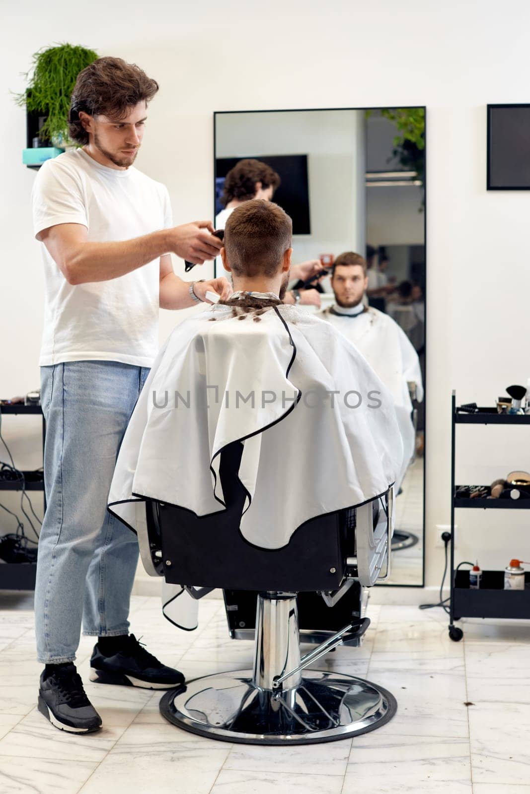 Barber trim hair with clipper on handsome bearded man in barber shop.