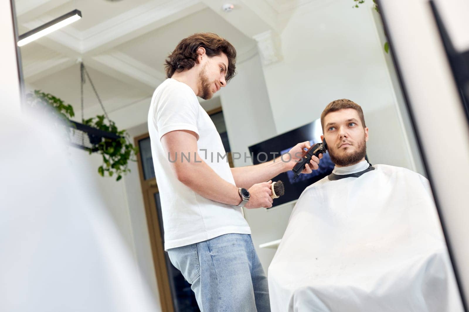 Barber trim hair with clipper on handsome bearded man in barber shop.