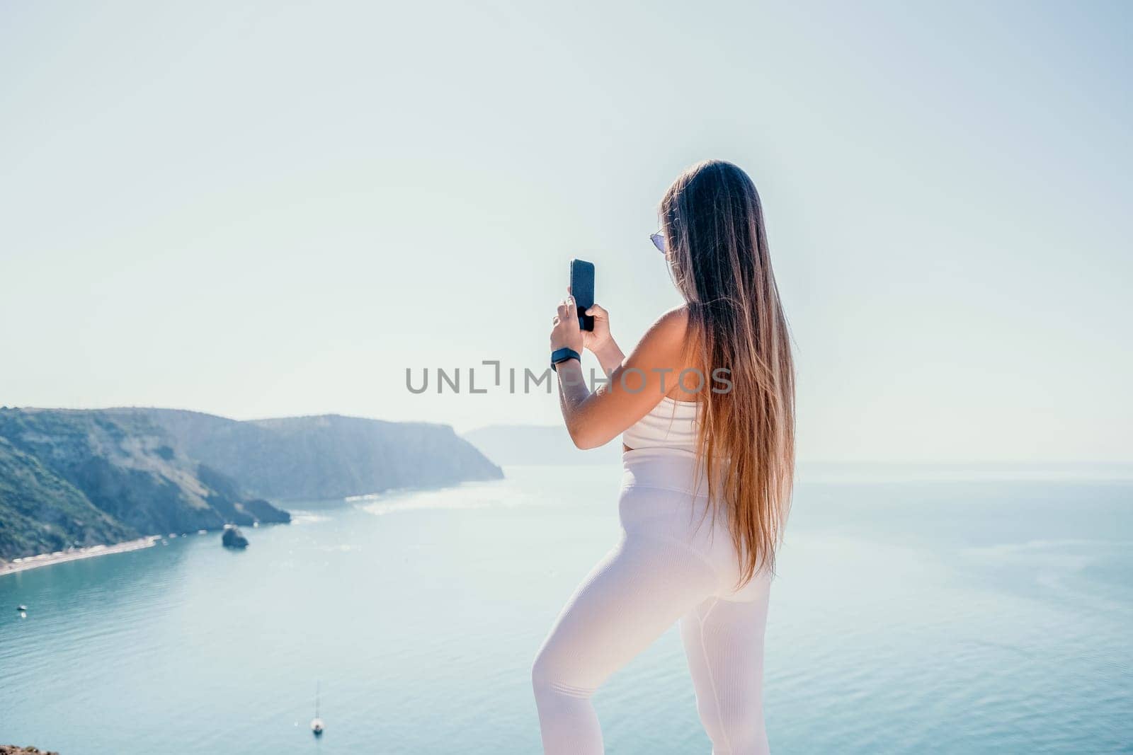 Digital nomad, woman in the hat, a business woman with a laptop sits on the rocks by the sea during sunset, makes a business transaction online from a distance. Freelance, remote work on vacation. by panophotograph