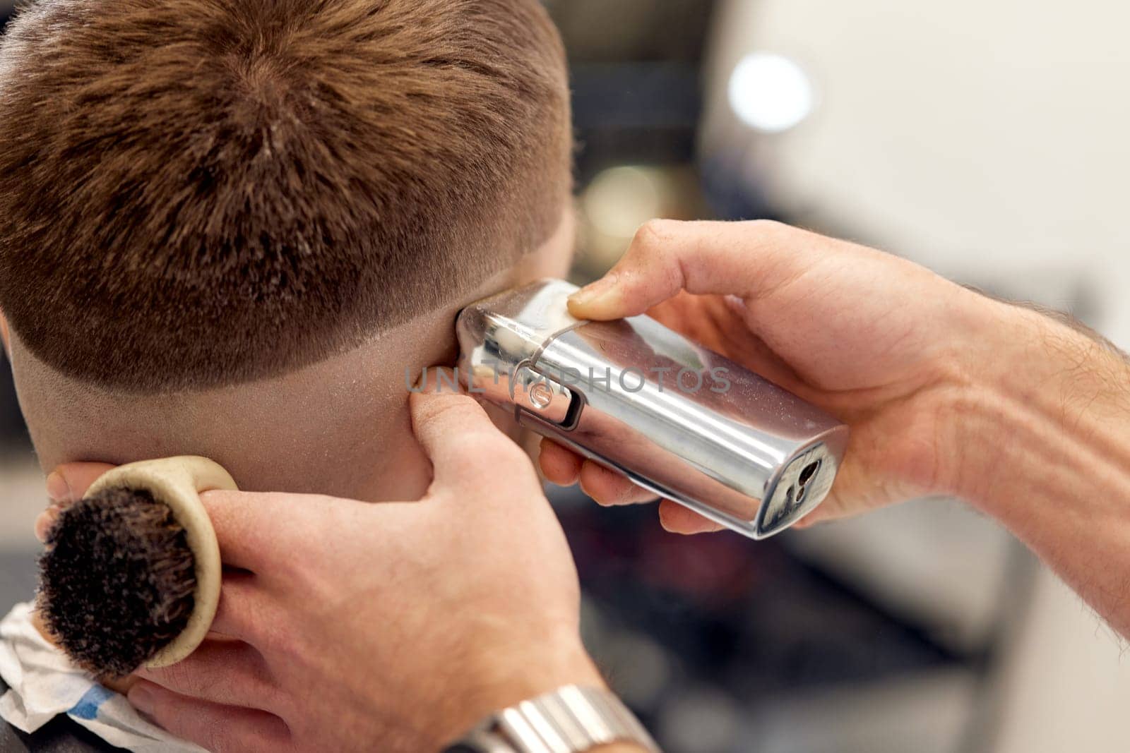 Barber trim hair with clipper on handsome bearded man in barber shop.