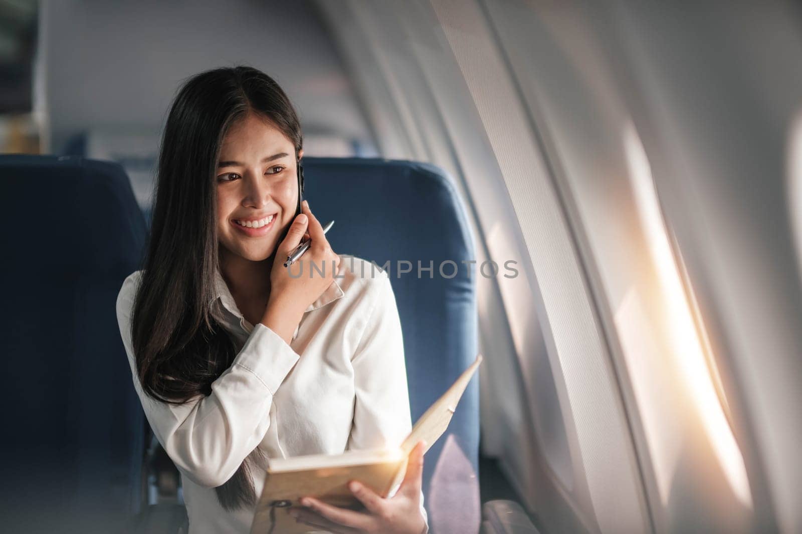 Asian young woman using smartphone and take notes in a notebook..sitting near windows at first class on airplane during flight,Traveling and Business concept..