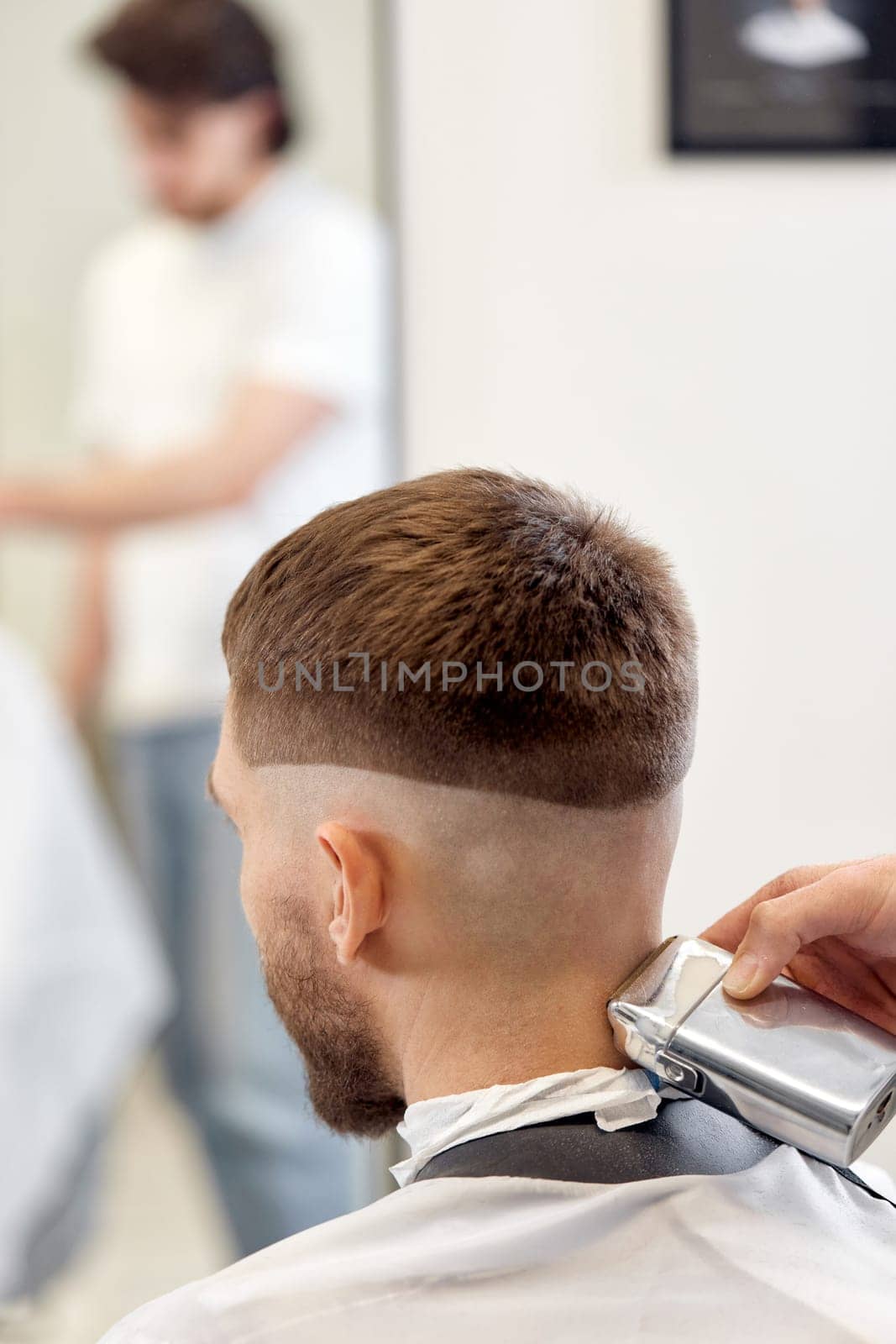 Barber trim hair with clipper on handsome bearded man in barber shop.