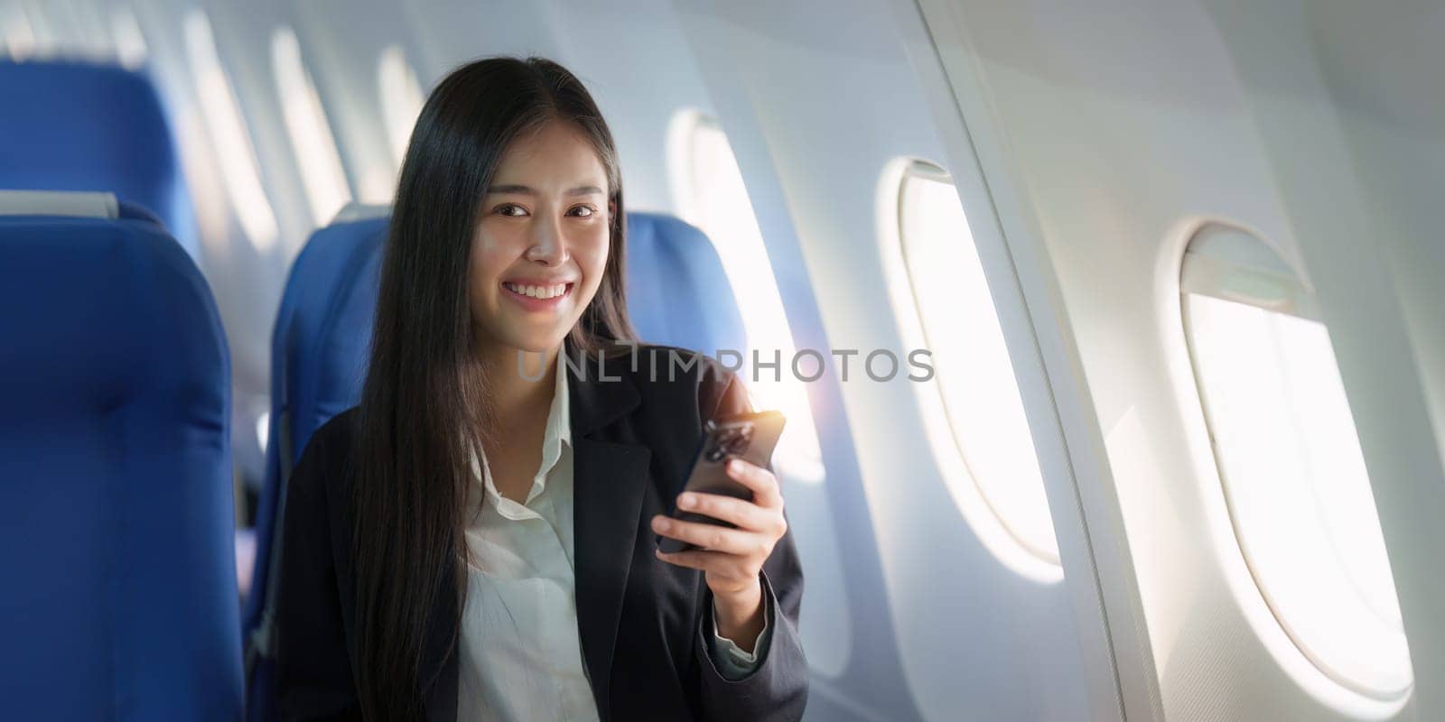 Beautiful Asian business woman chatting with client by mobile phone during flight. working, travel, business concept by itchaznong