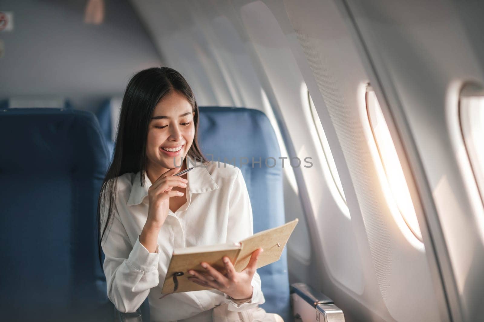 Asian young woman take notes in a notebook sitting near windows at first class on airplane during flight,Traveling and Business concept..