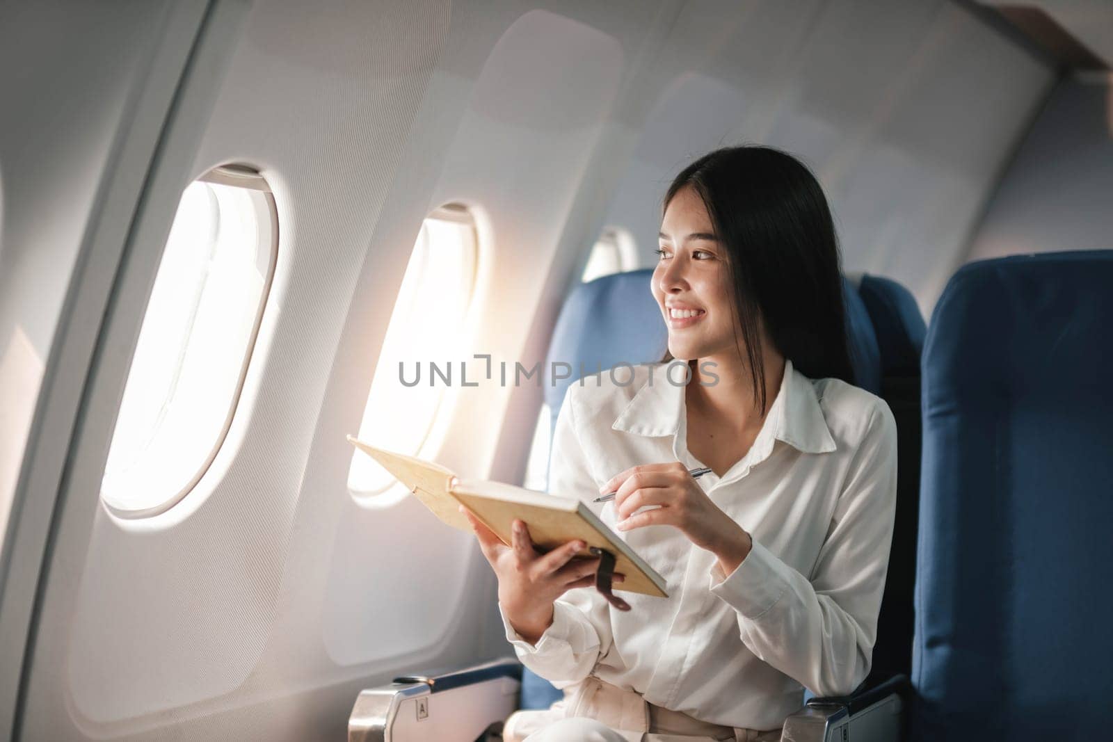 Asian young woman take notes in a notebook sitting near windows at first class on airplane during flight,Traveling and Business concept..