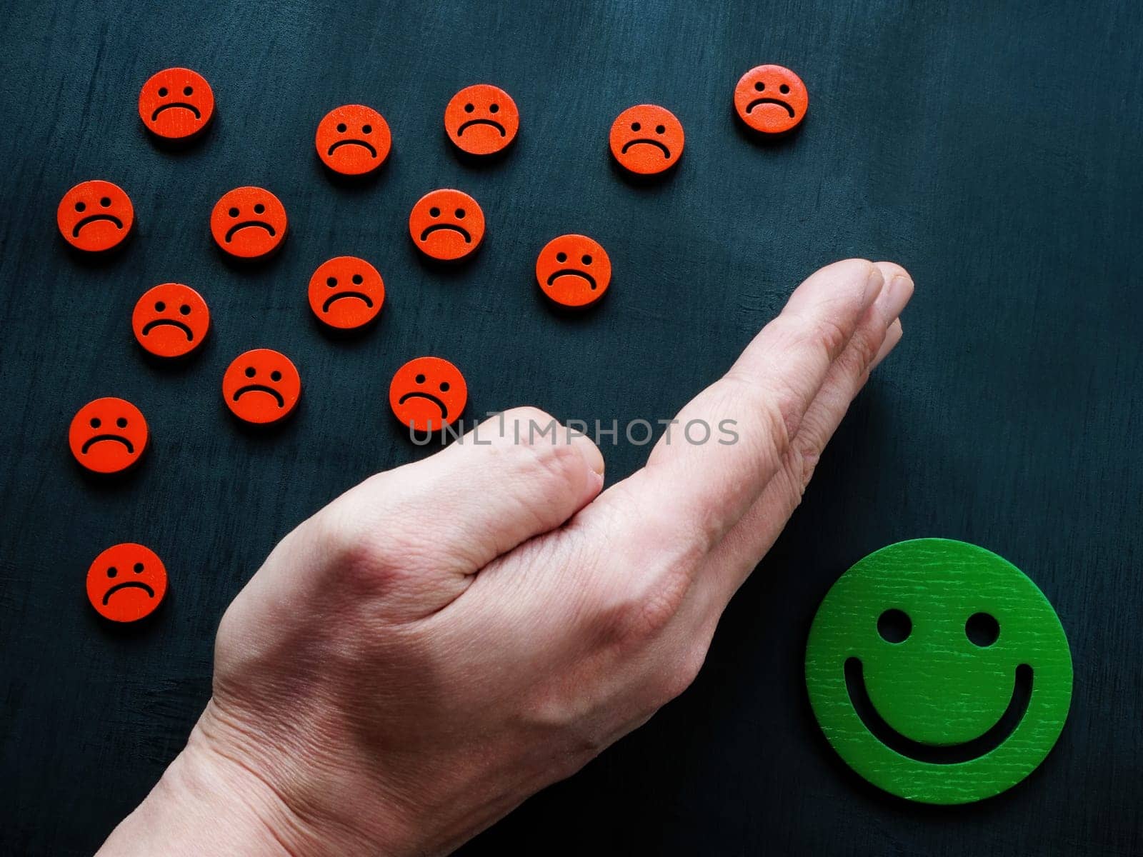 The hand protects the joyful emoticon from the sad ones. Emotional regulation concept. by designer491