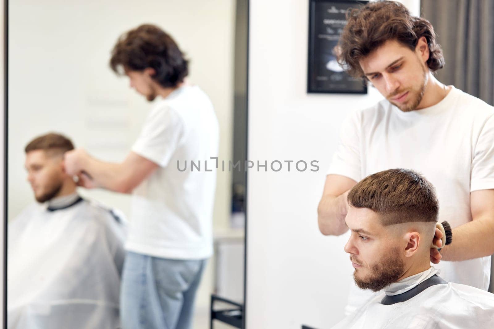 Barber trim hair with clipper on handsome bearded man in barber shop.
