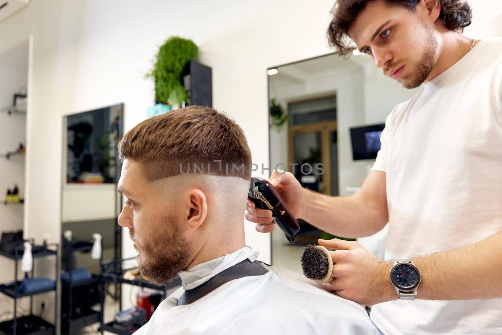 Barber trim hair with clipper on handsome bearded man in barber shop.