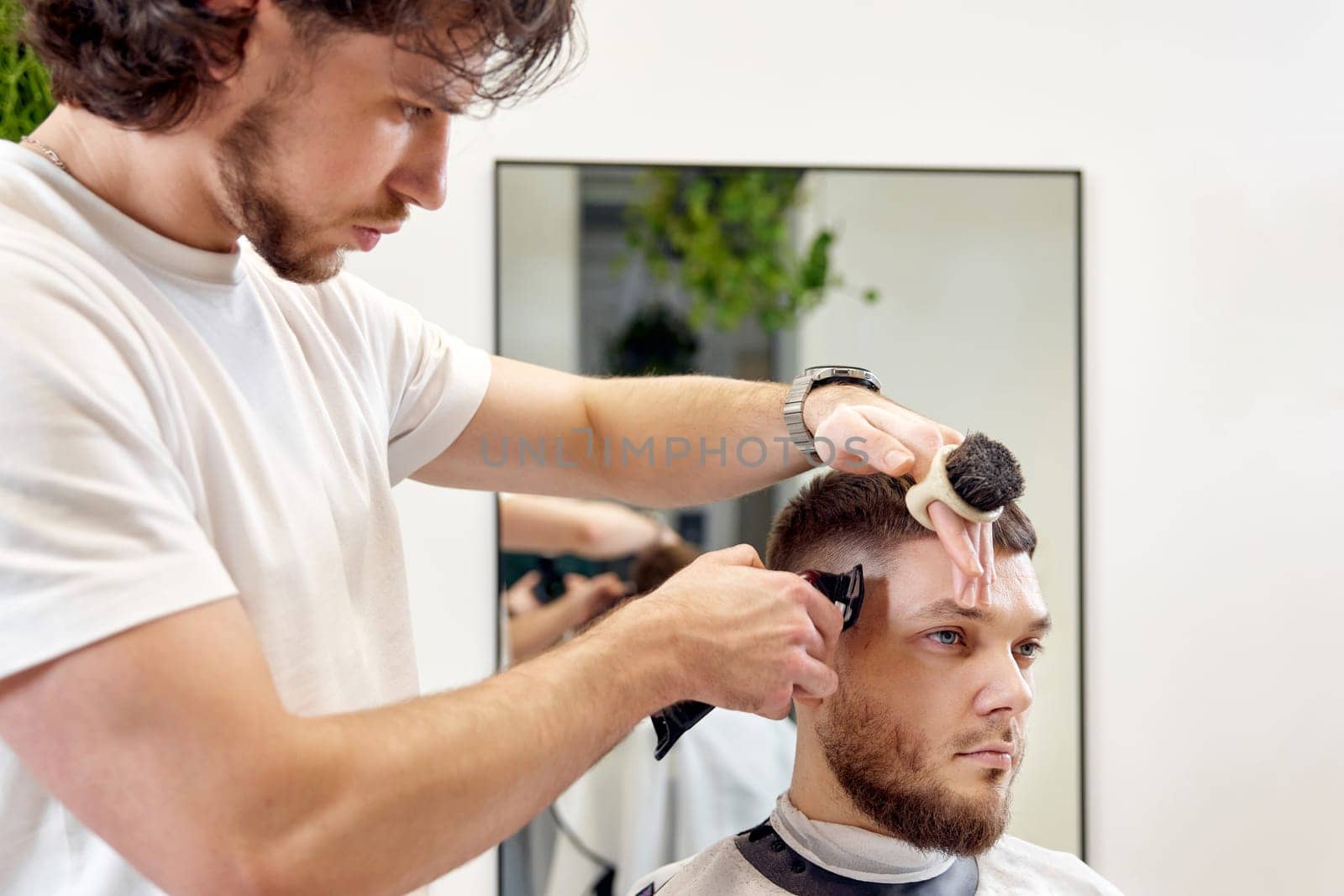 Barber trim hair with clipper on handsome bearded man in barber shop.