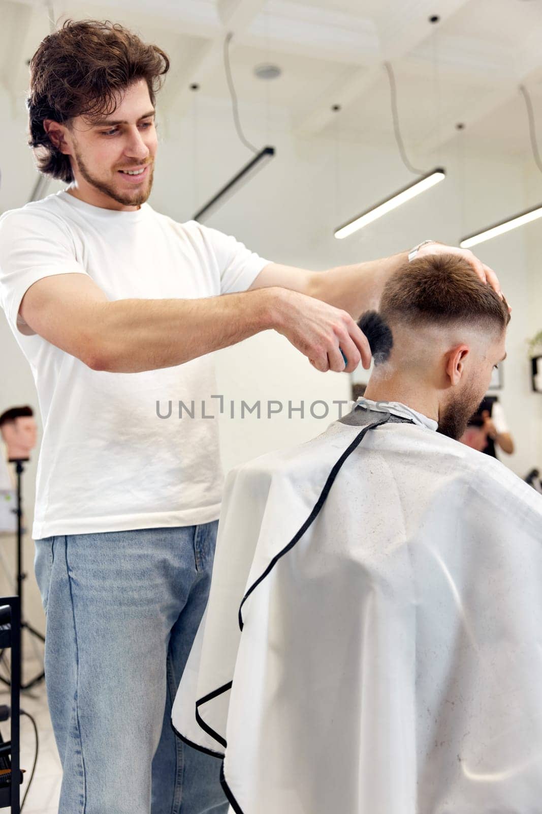 Barber trim hair with clipper on handsome bearded man in barber shop.