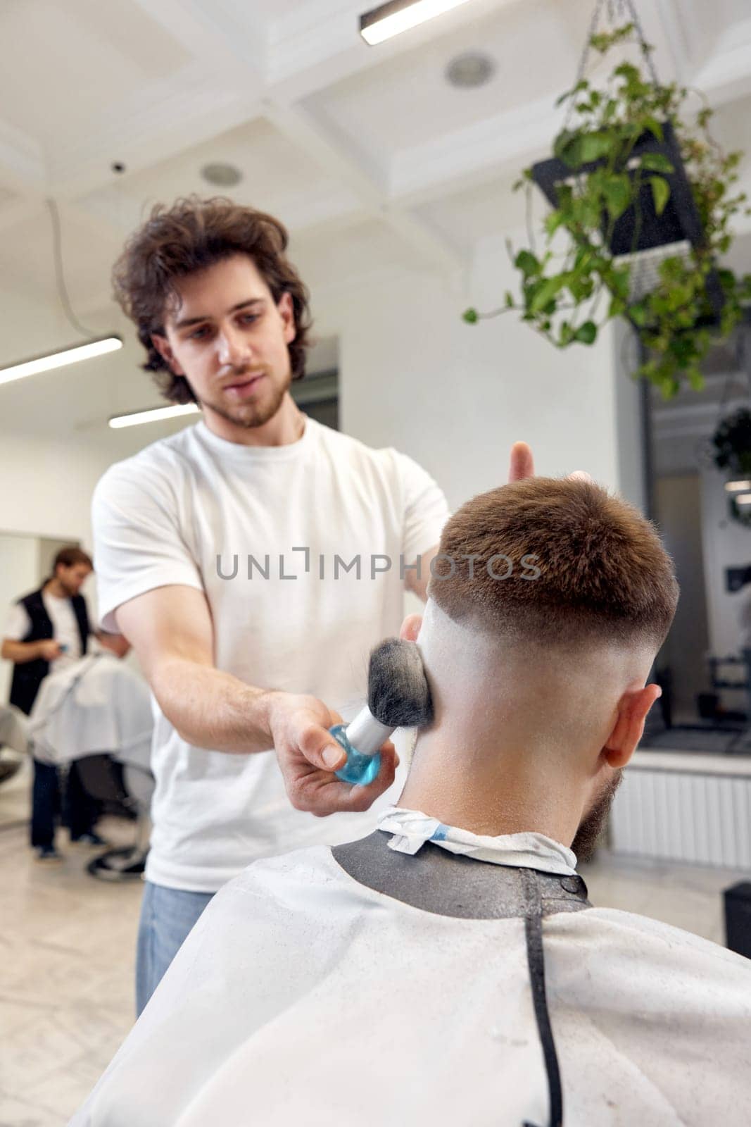 Barber trim hair with clipper on handsome bearded man in barber shop.