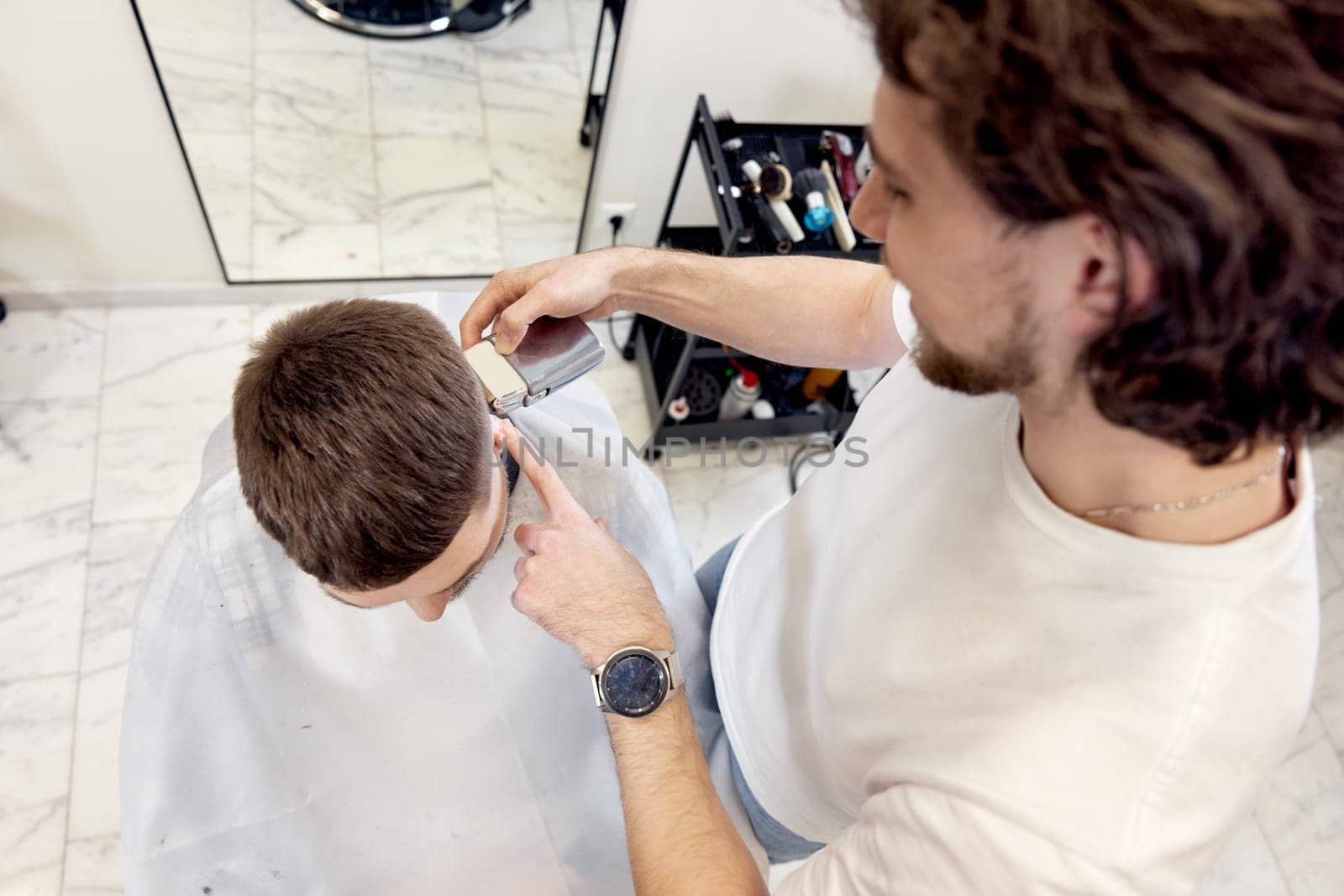 Barber trim hair with clipper on handsome bearded man in barber shop.