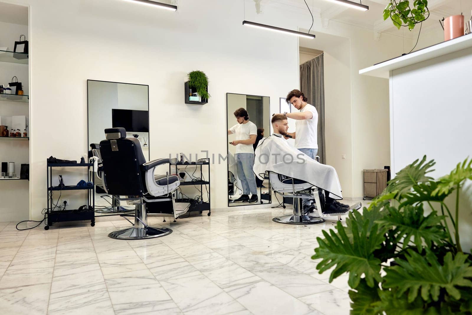 Professional barber during work with man client in modern light barber shop.