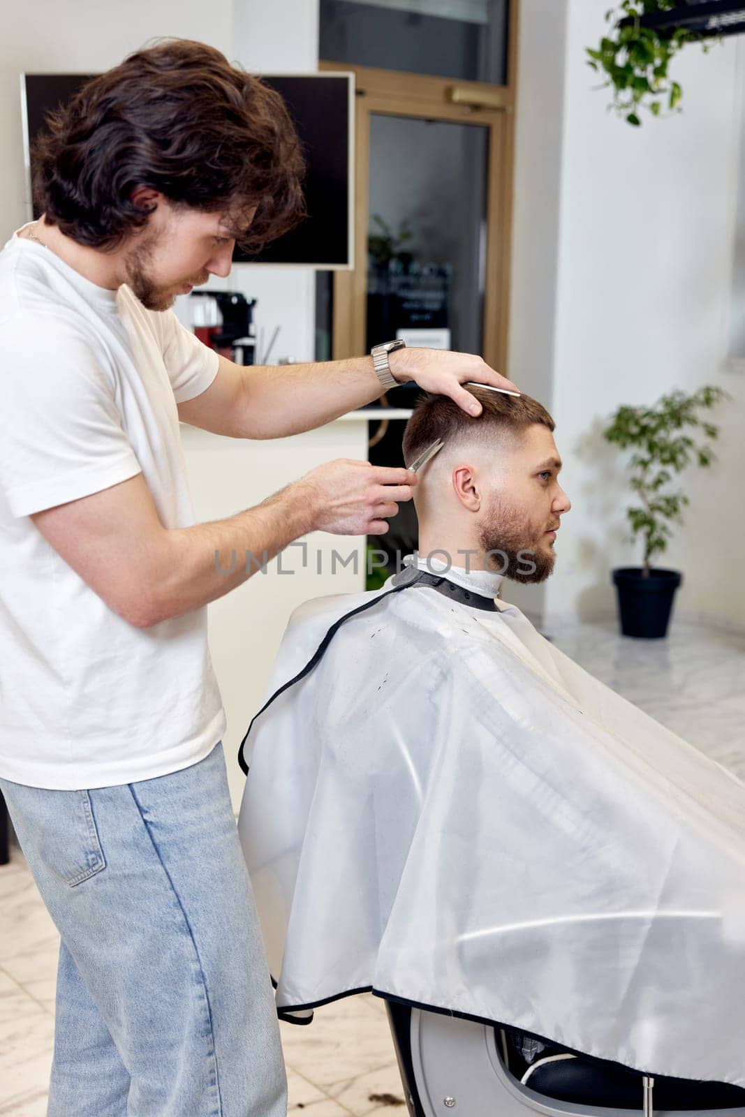 Barber trim hair with clipper on handsome bearded man in barber shop.