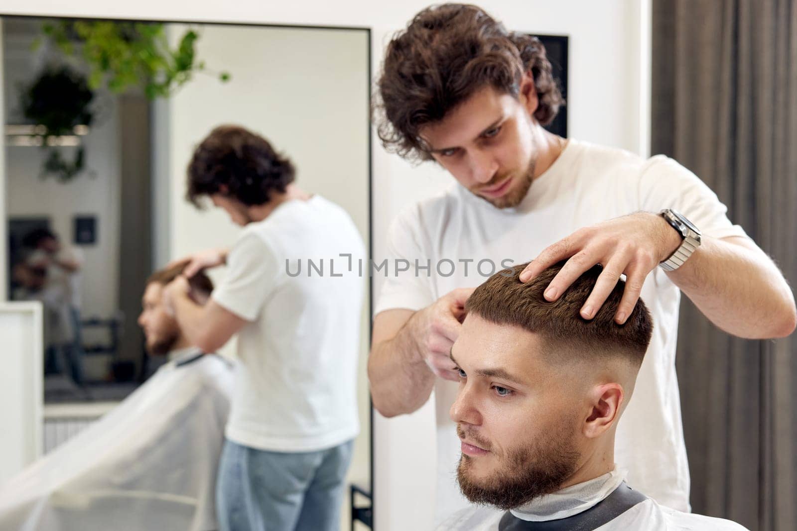 Barber trim hair with clipper on handsome bearded man in barber shop.