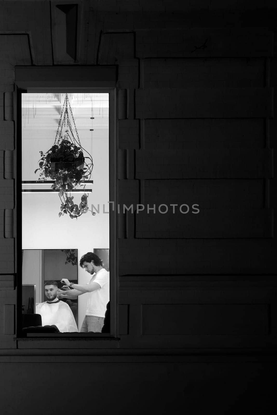 Hairstylist serving handsome bearded man in barber shop. the view from outdoor