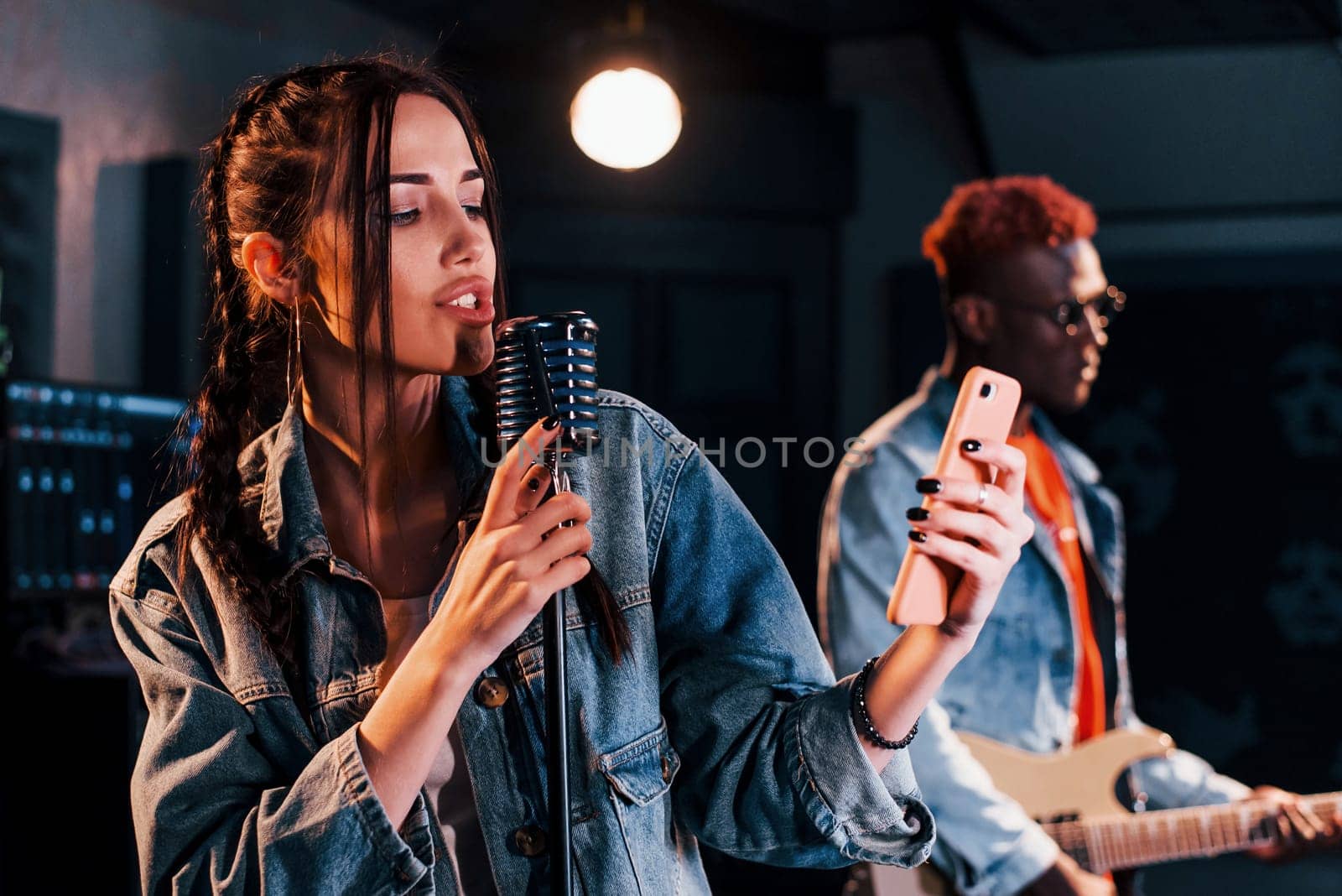 Guy plays guitar, girl sings. African american man with white girl rehearsing in the studio together.
