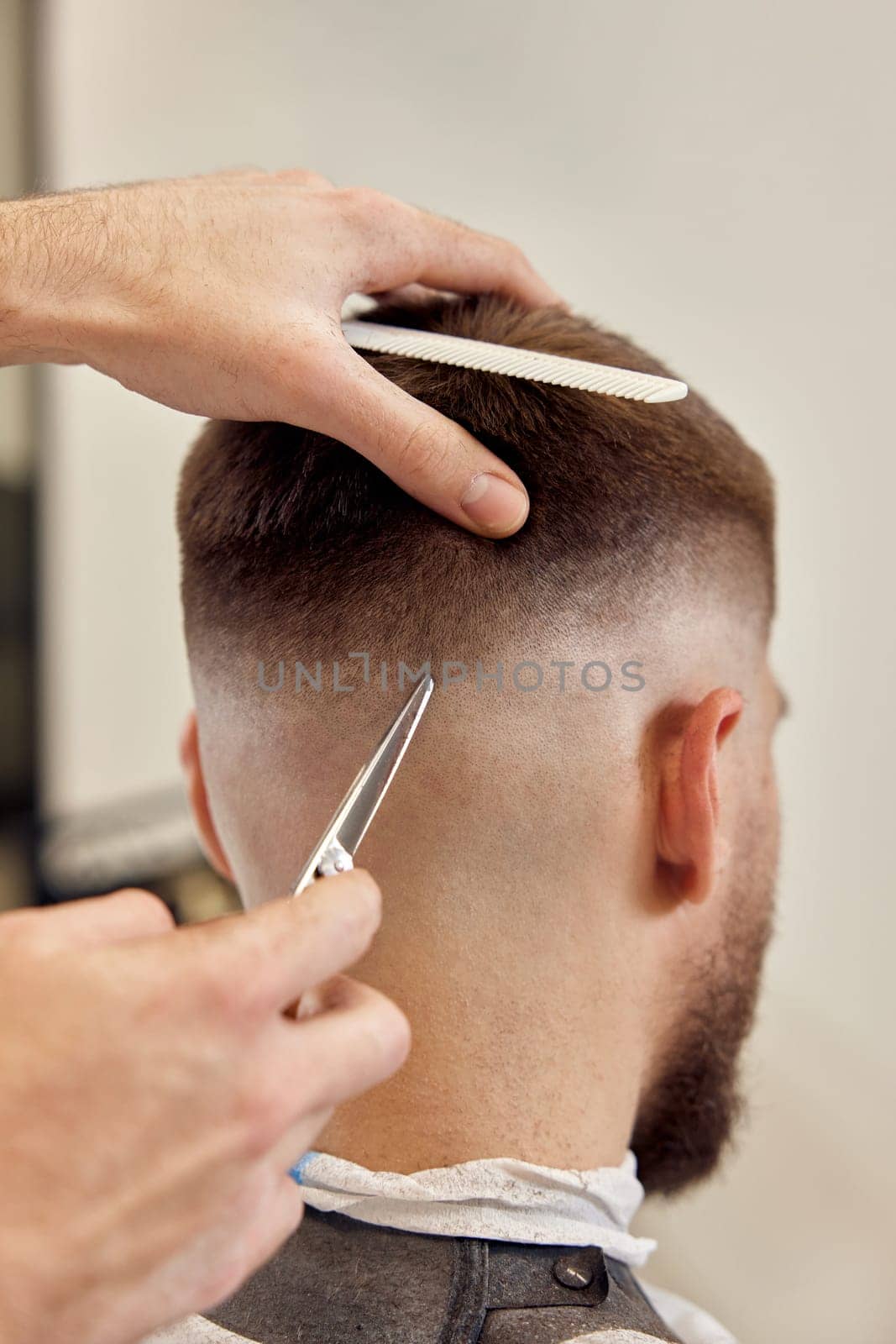 barber does haircut for caucasian bearded man using comb and scissors at barber shop. close-up