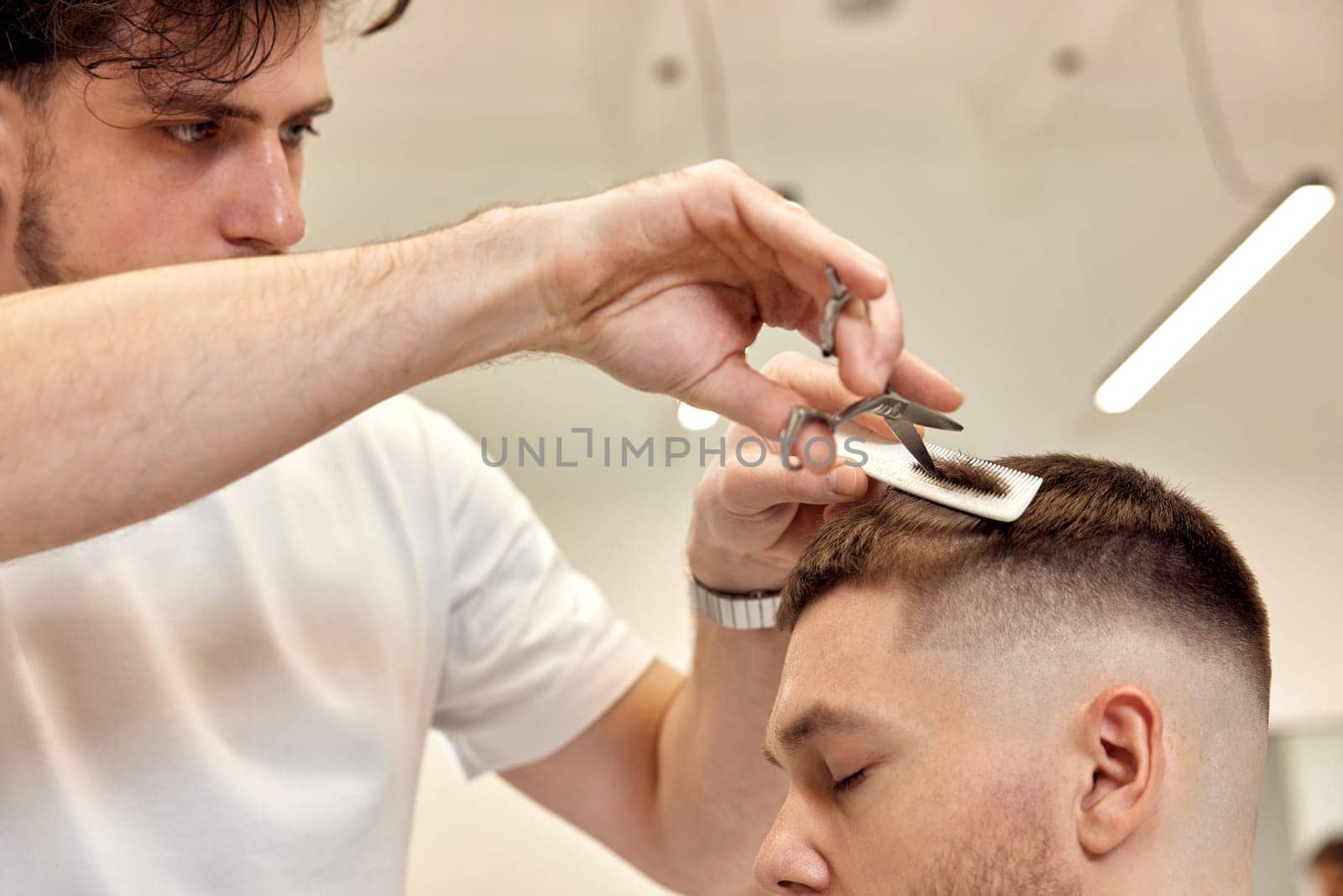 barber does haircut for caucasian bearded man using comb and scissors at barber shop. close-up