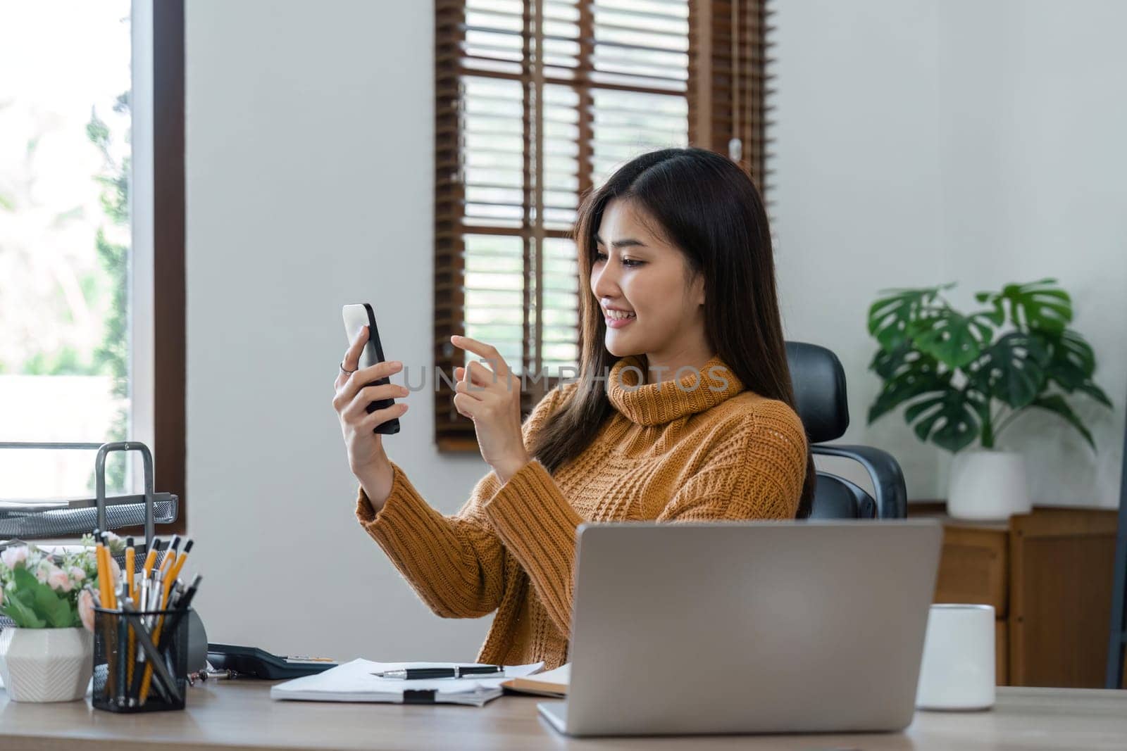 business woman with phone for communication, connection and typing while smile, happy and relax. Entrepreneur, excited and with laptop for planning at home.