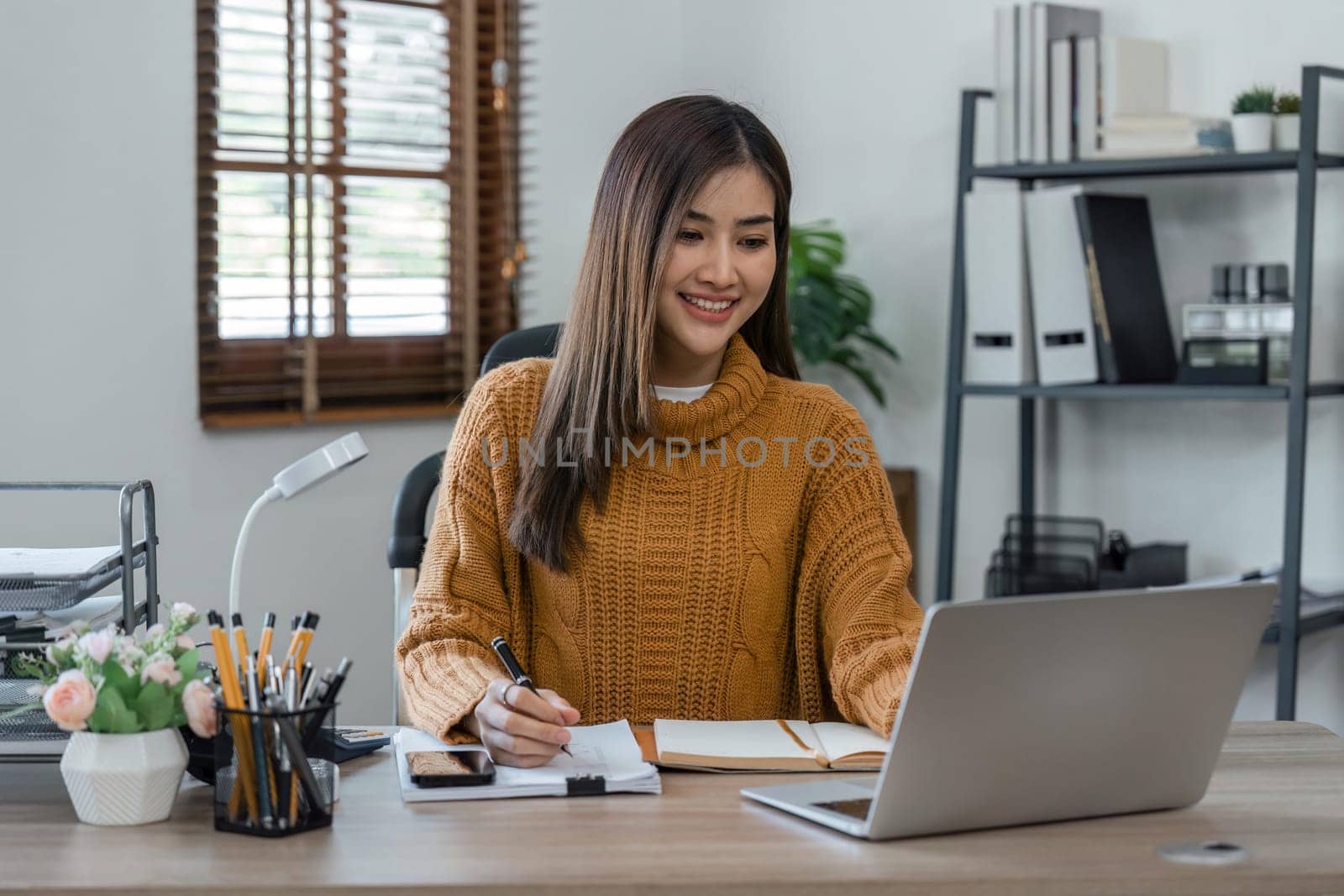 Shot of young asian woman working at home with laptop and documents.