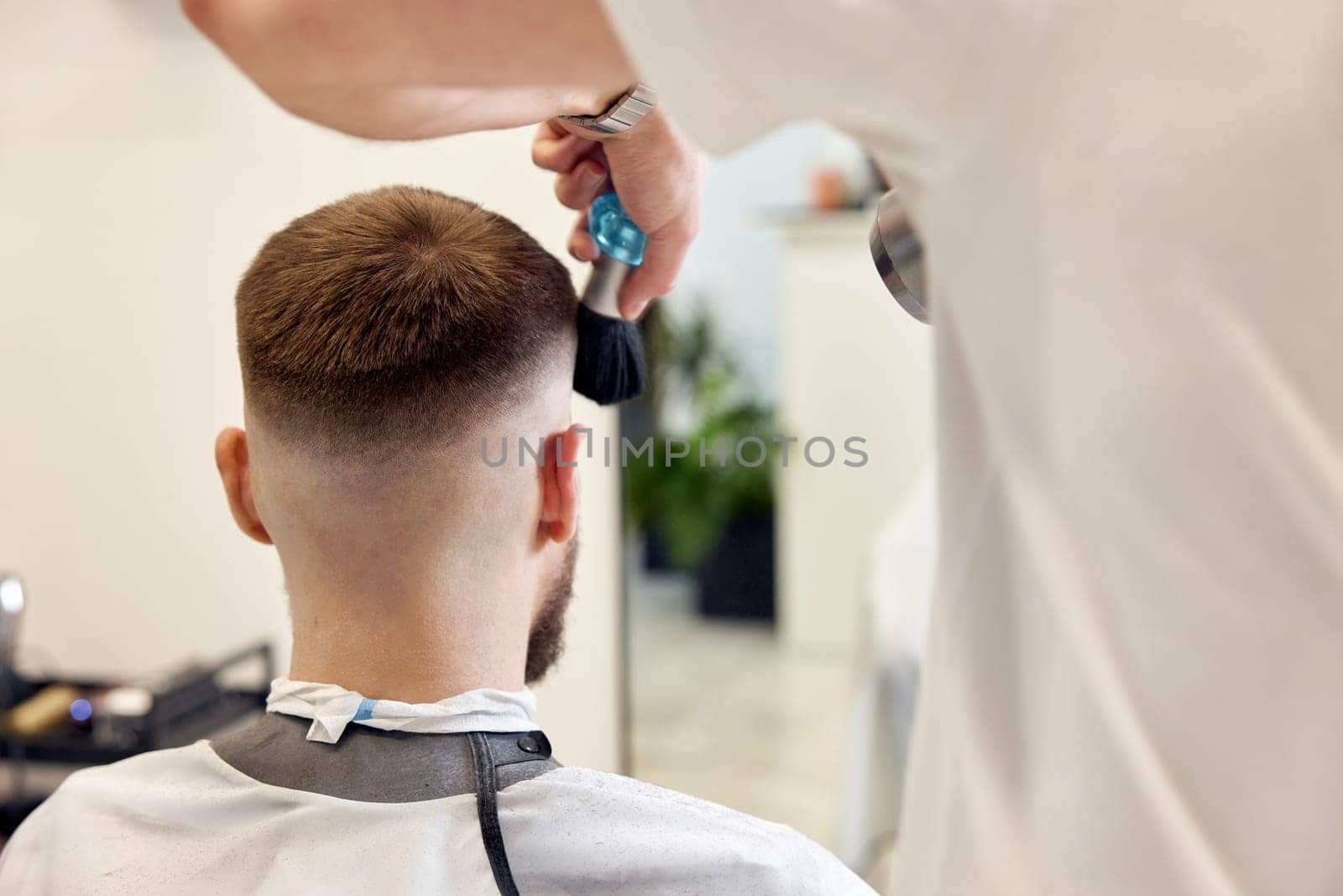 Hairstylist serving handsome bearded man in barber shop.