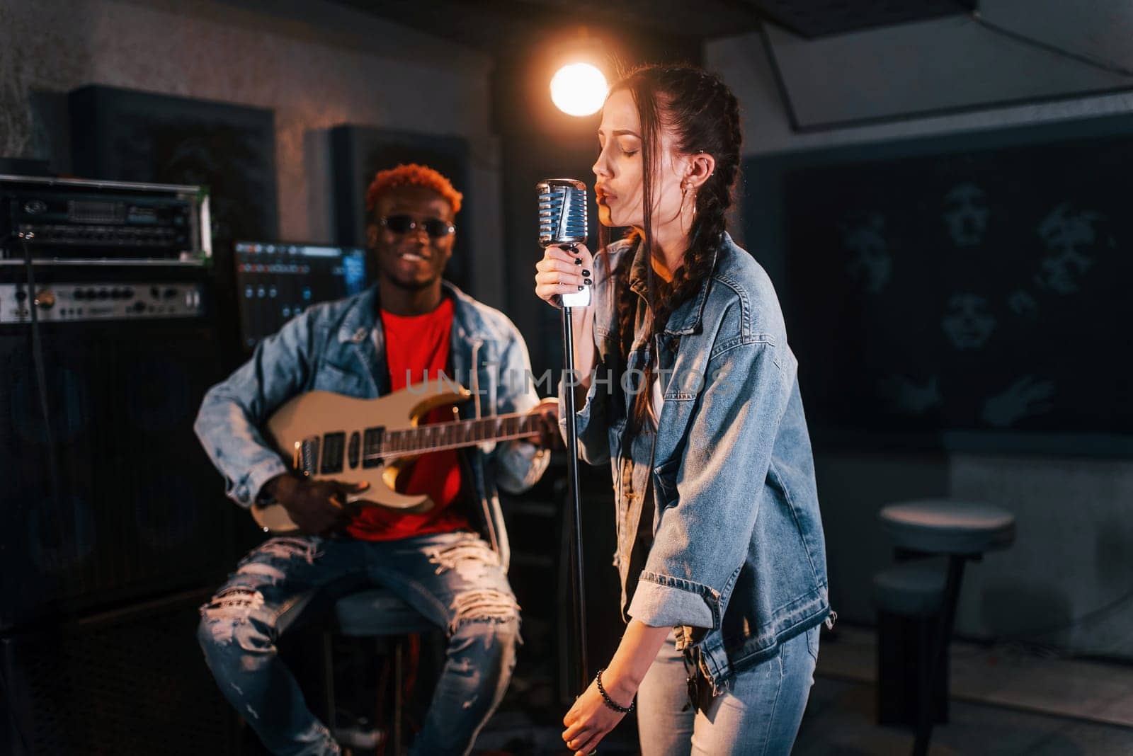 Guy plays guitar, girl sings. African american man with white girl rehearsing in the studio together by Standret