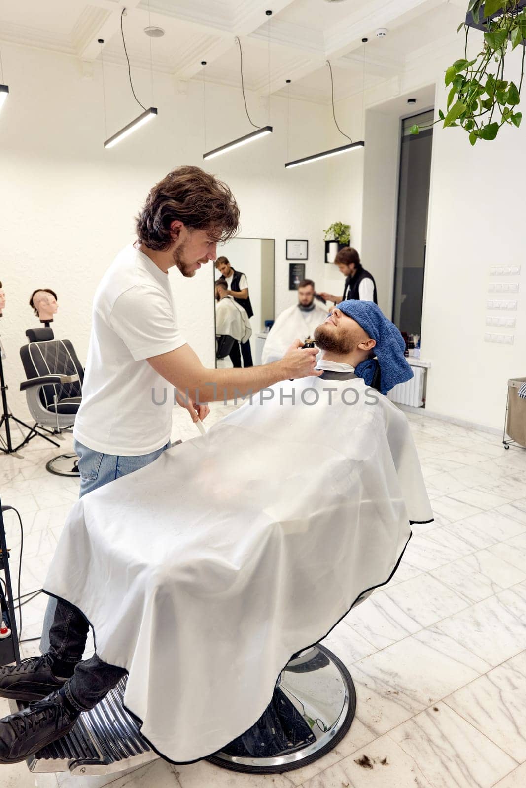 Barber shaving handsome bearded man in barber shop.