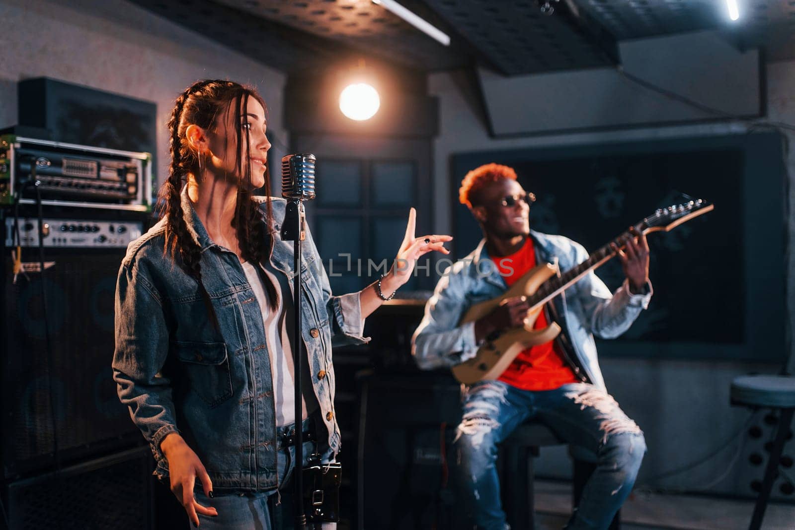 Guy plays guitar, girl sings. African american man with white girl rehearsing in the studio together.