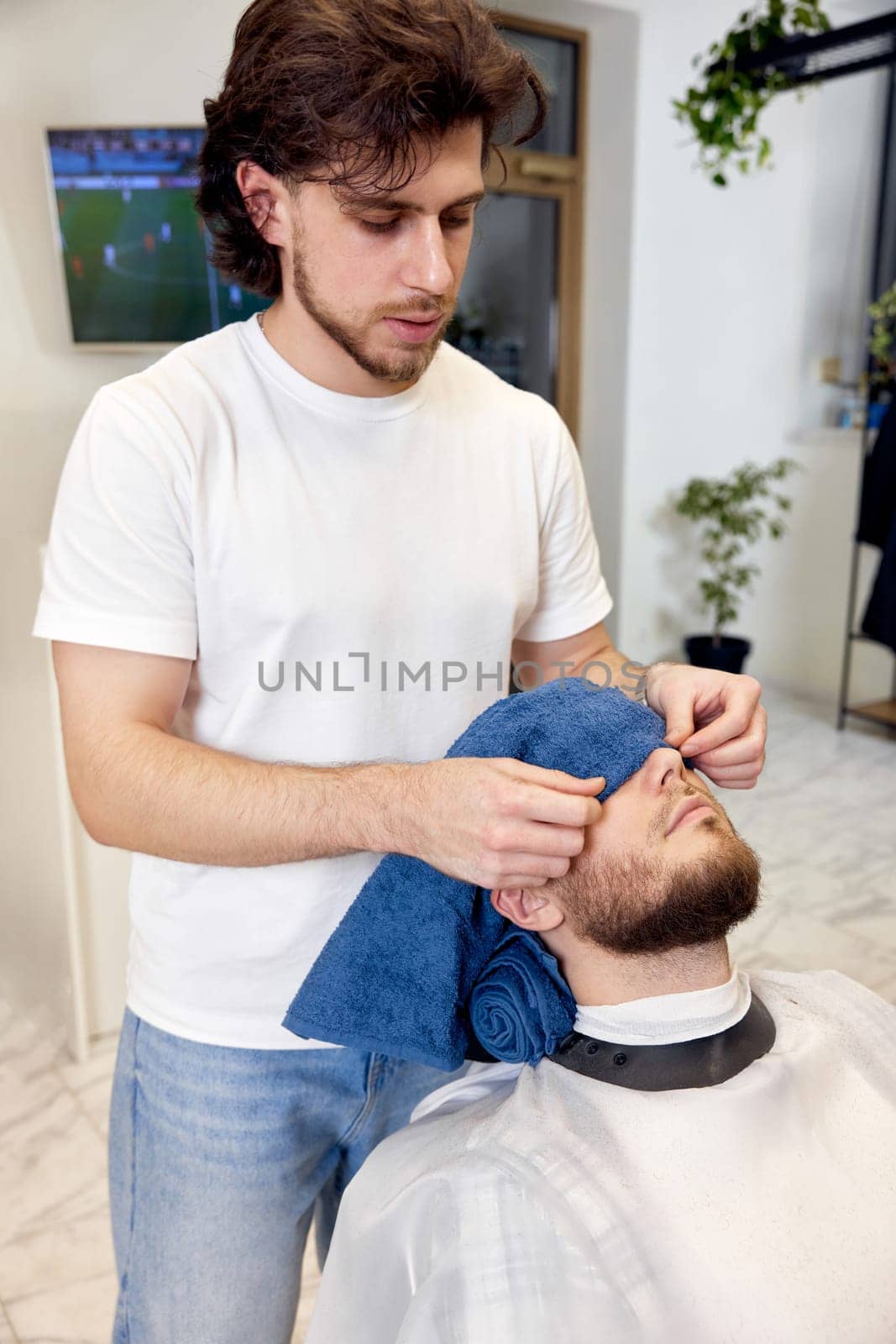 Barber shaving bearded man in barber shop. by erstudio