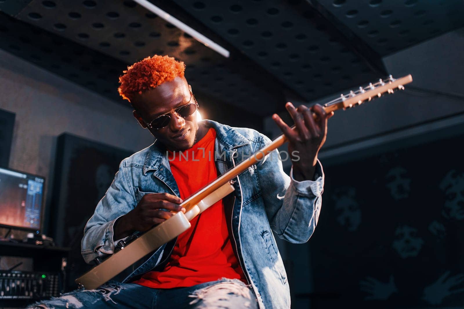 Plays guitar. Young african american performer rehearsing in a recording studio by Standret