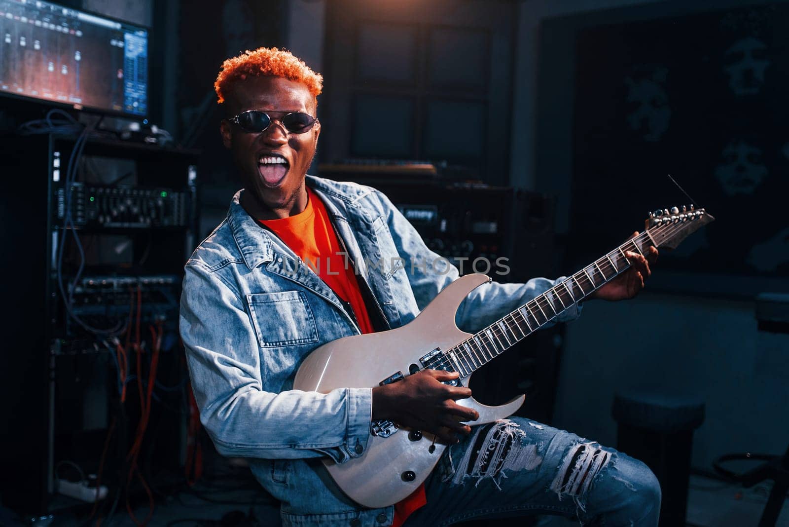 Plays guitar. Young african american performer rehearsing in a recording studio.