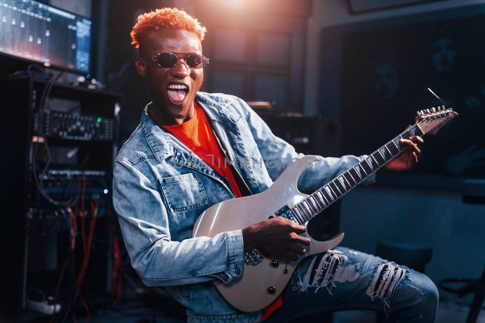 Plays guitar. Young african american performer rehearsing in a recording studio by Standret