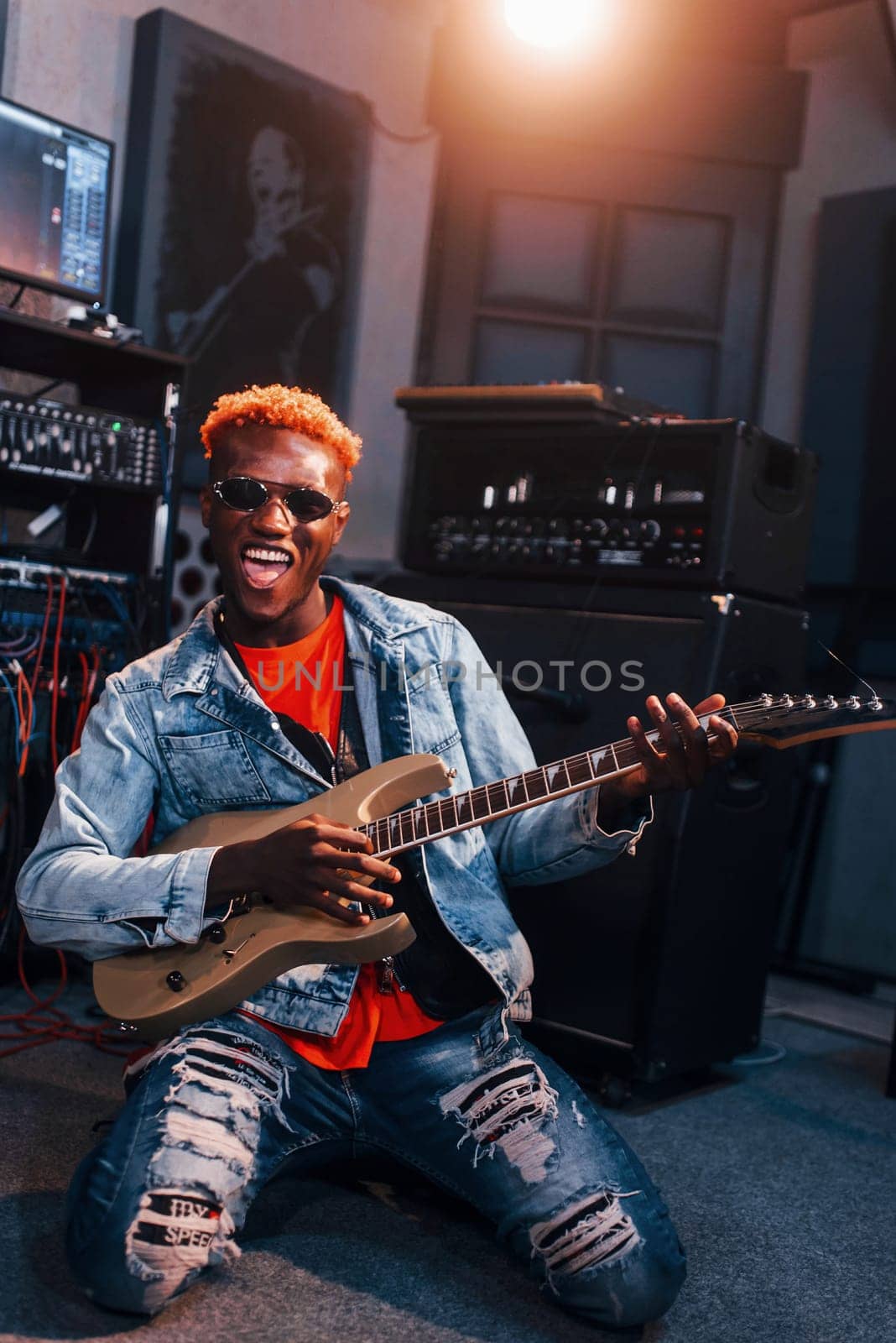 Plays guitar. Young african american performer rehearsing in a recording studio.