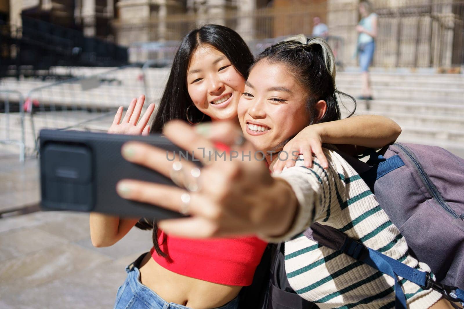 Delighted Asian women taking self portrait on smartphone and smiling during trip by javiindy