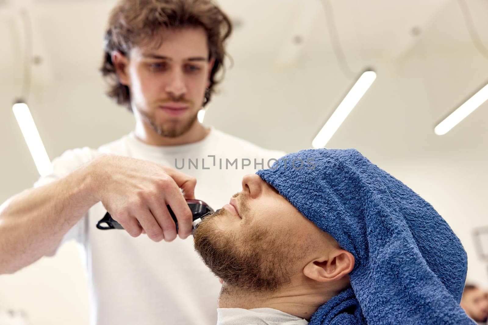 Barber shaving handsome bearded man in barber shop.