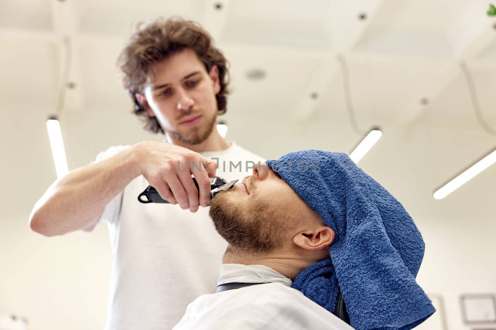 Barber shaving bearded man in barber shop. by erstudio