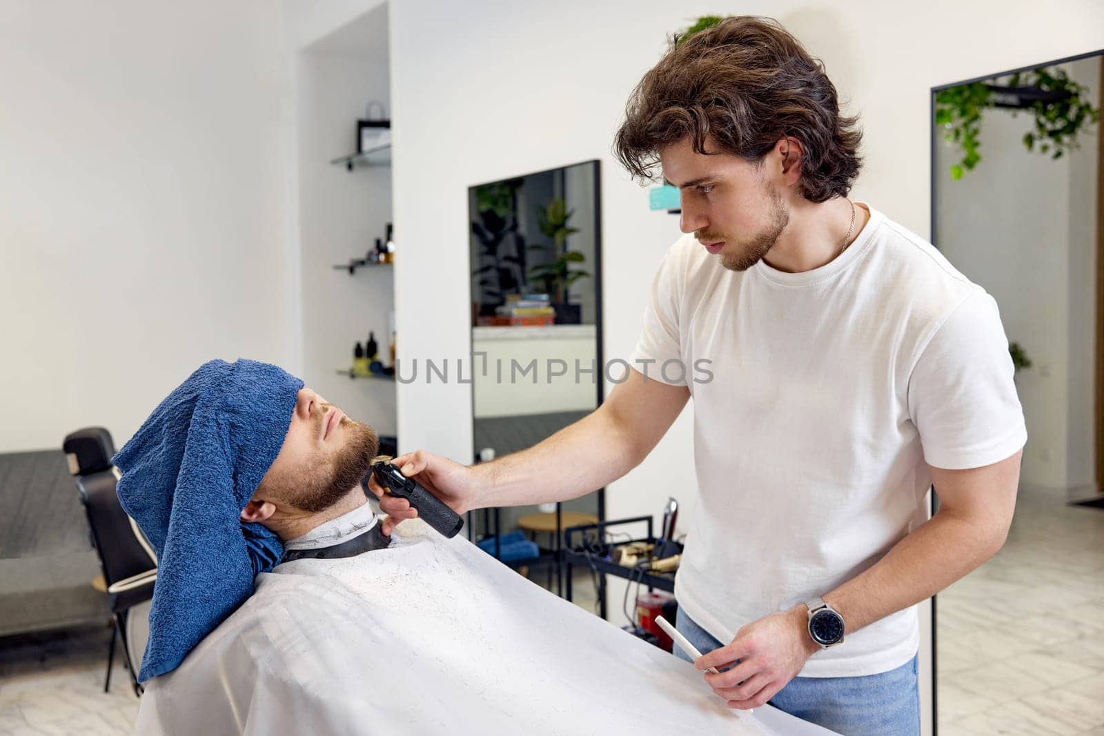 Barber shaving handsome bearded man in barber shop.