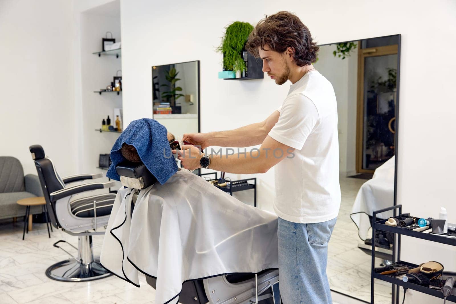 Barber shaving handsome bearded man in barber shop.