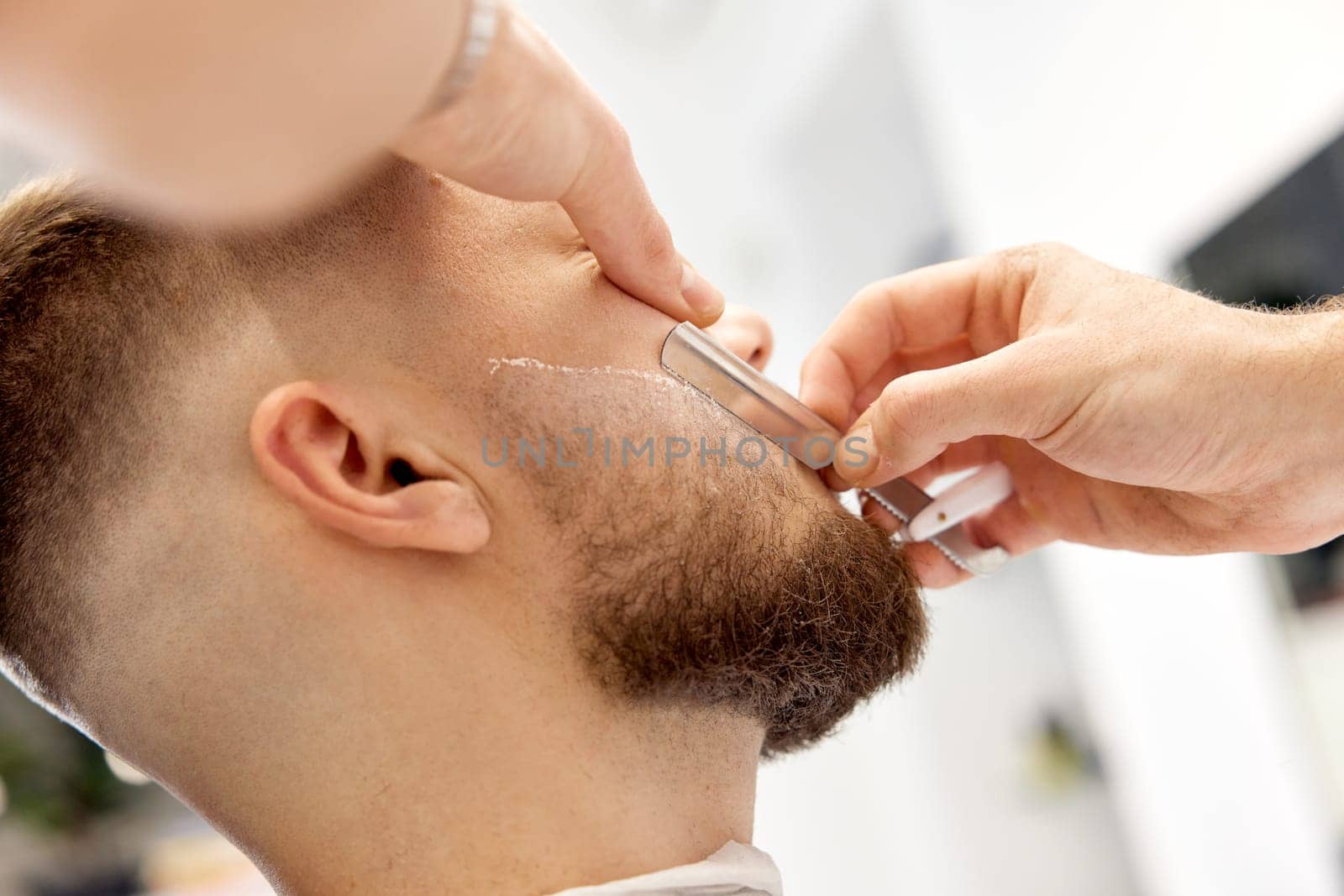 Barber shaving bearded man with retro knife in barber shop. close-up