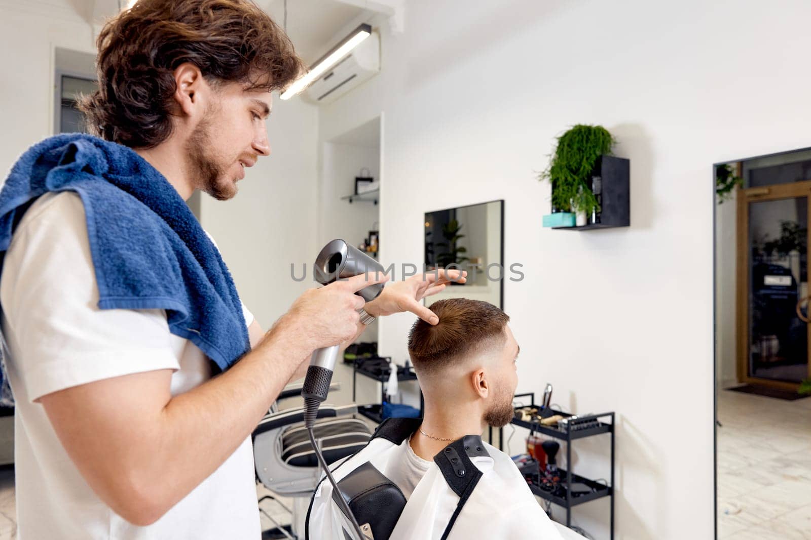 Professional hairdresser during work with man client with hair dryer in barber shop. Haircut in the barbershop.