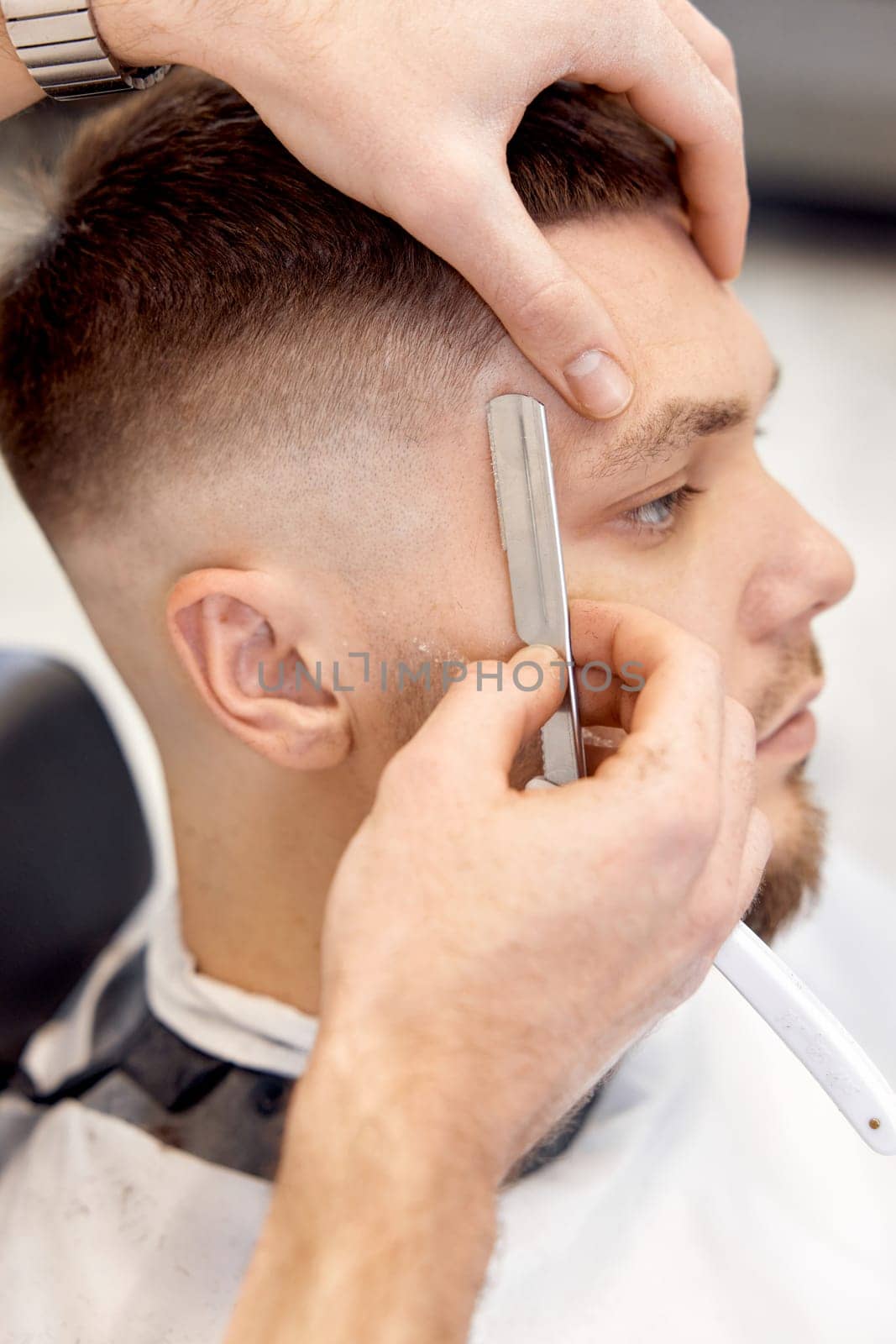 Barber shaving bearded man with retro knife in barber shop. close-up
