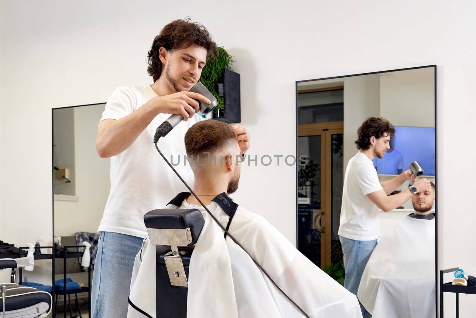 Professional hairdresser during work with man client with hair dryer in barber shop. Haircut in the barbershop.